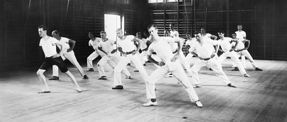 En grupp män gymnastiserar i en gymnastikhall på tidigt 1900-tal