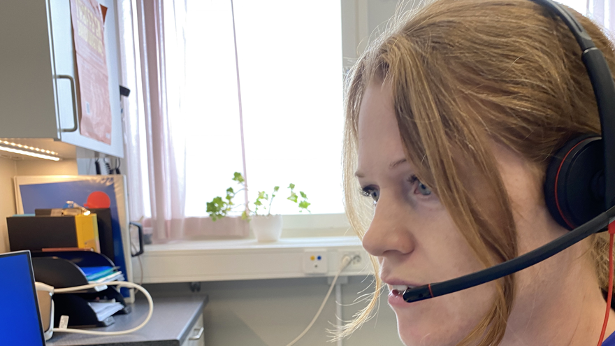 Person i vårdkläder med headset framför dator.