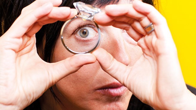 Kvinna tittar genom förstoringsglas vilket gör henne öga stort
