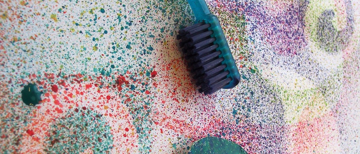 Olika färger är stänkt i olika mönster. En tandborste ligger på målningen.