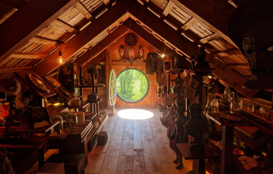 Ett runt fönster öppet mot grönskan längst in i en dunkel vind fylld av samlingar av olika slag.