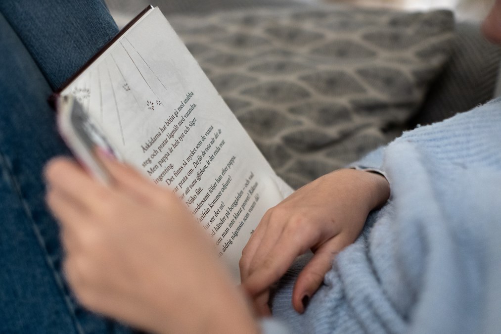 Barn som sitter med en bok i knät hon läser ur.