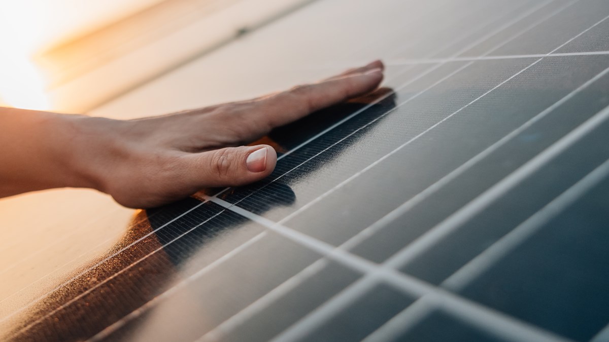 Hand som vilar på solceller med sol i bakgrunden