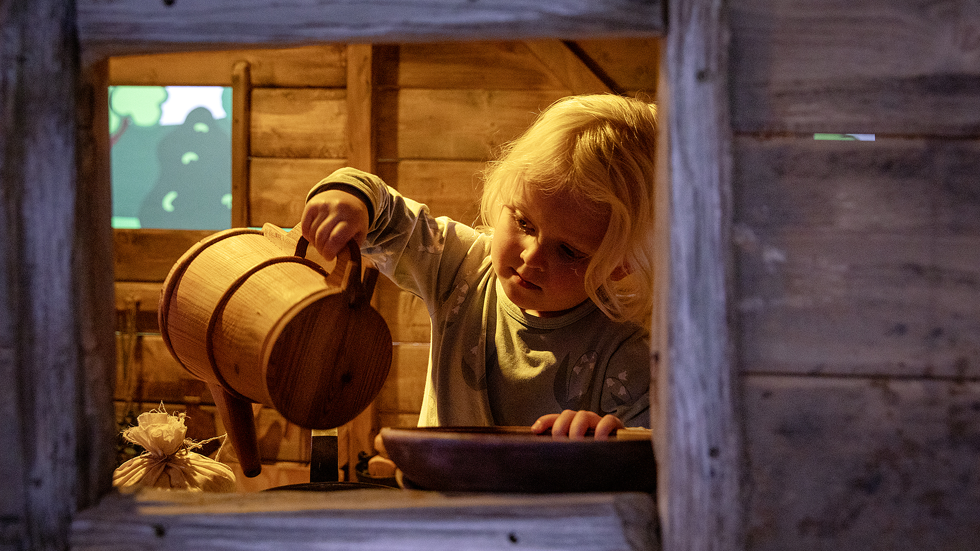 Ett barn i 4-årsåldern leker med en kanna som hon ser ut att hälla något från i en lekstugemiljö