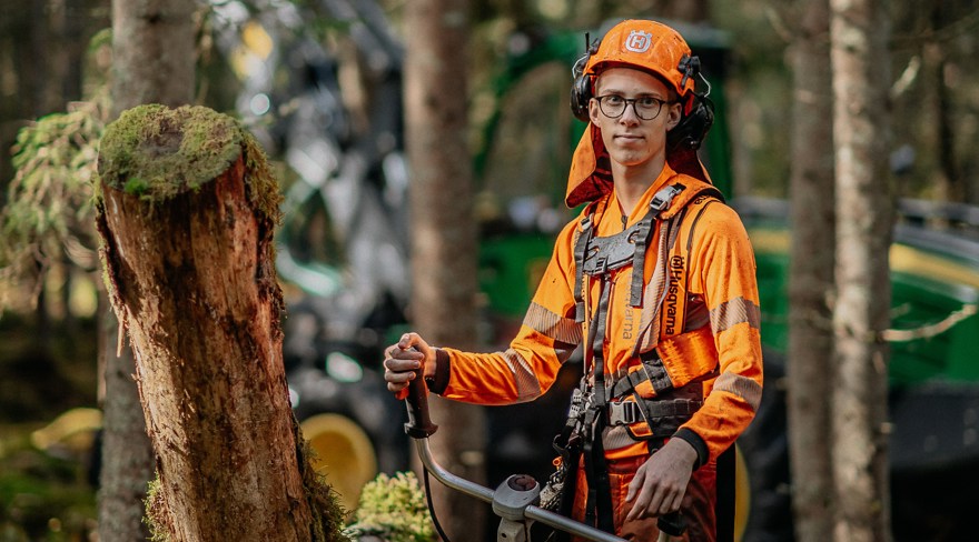 Elev med skyddskläder och hjälm står i skogen och håller i röjsåg