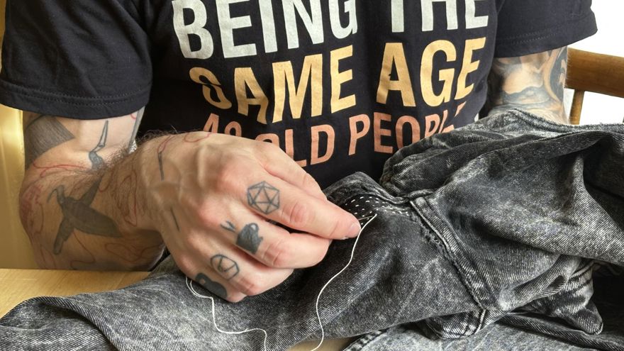 En person med tatuerade händer syr på ett par jeans
