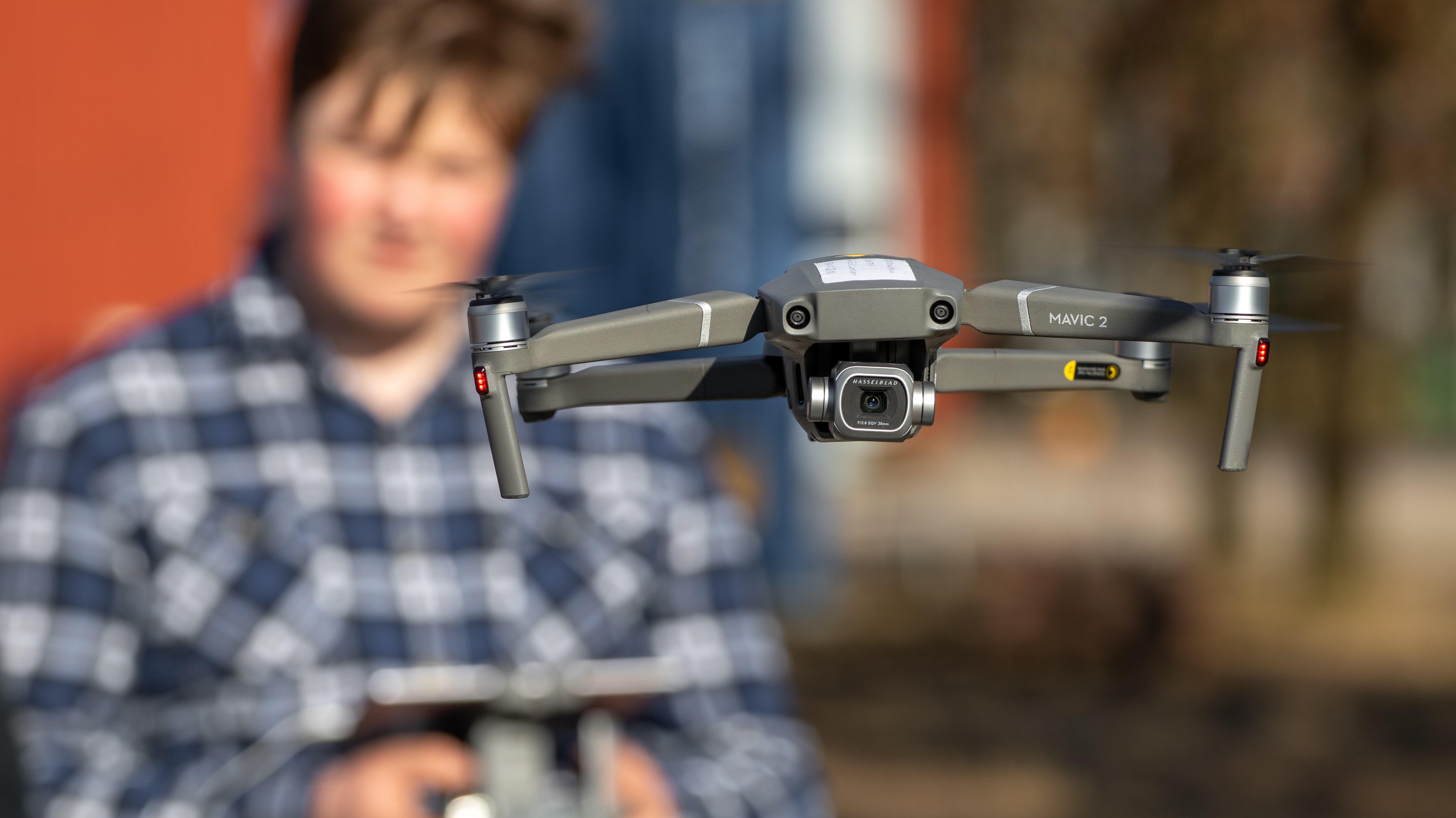 Närbild på flygande drönare med elev i bakgrunden som håller i fjärrkontroll
