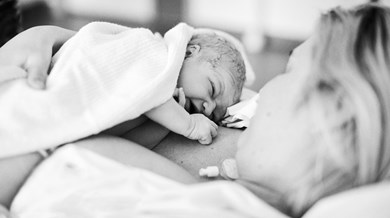 En nyfödd bebis ligger på sin mammas mage insvept i en filt.
