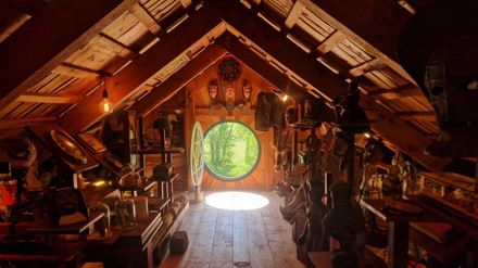 Ett runt fönster öppet mot ljus och grönska längst in i en dunkel vind fylld med samlingar