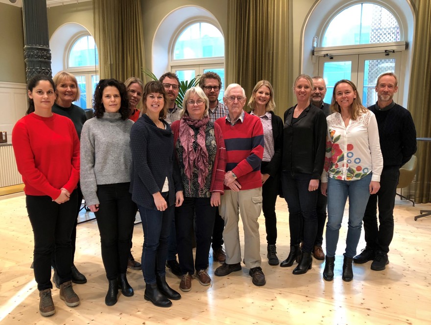 14 kvinnor och män som står tillsammans i ett konferensrum