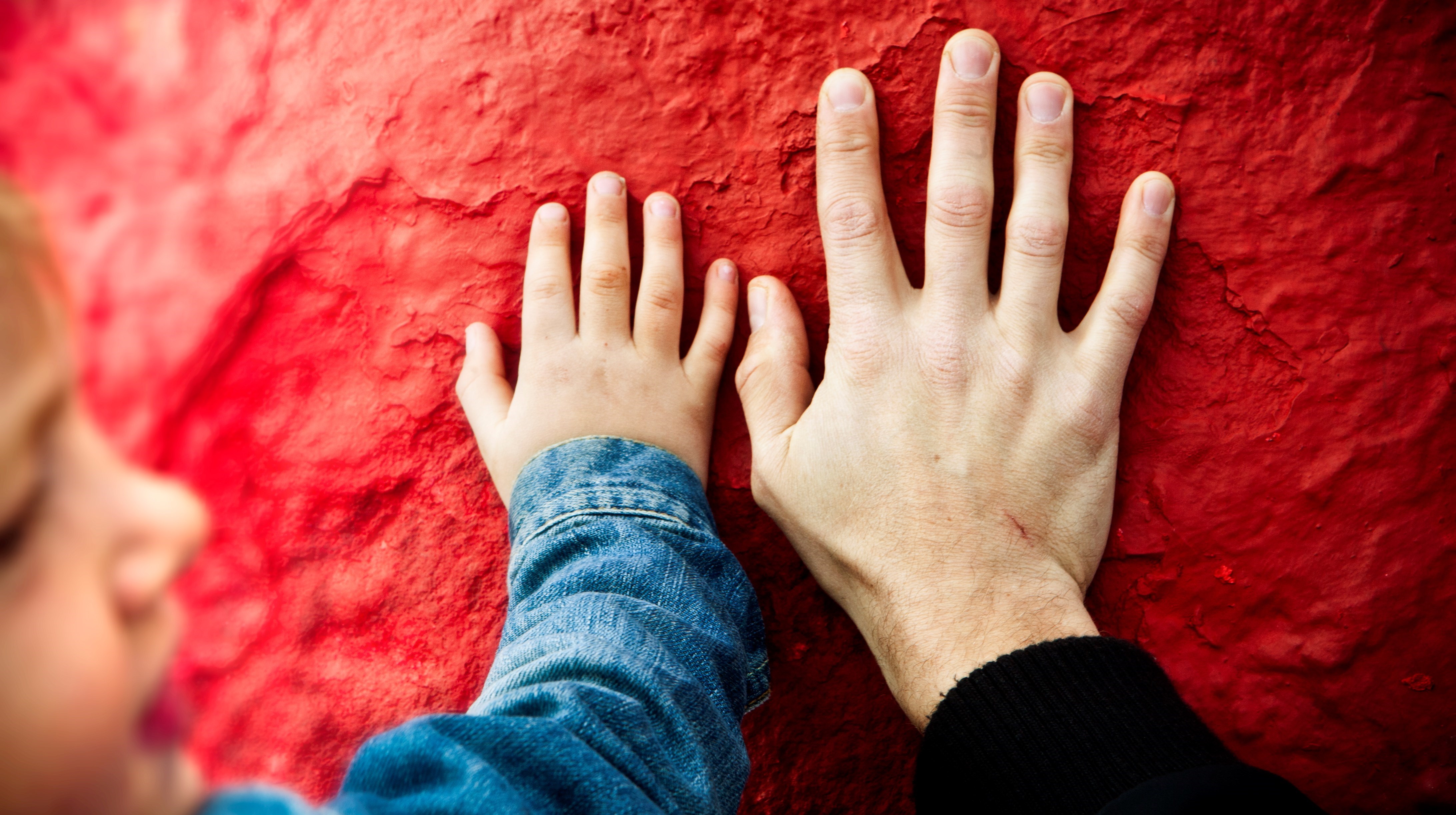 en barnhand och en vuxenhand bredvid varandra mot en röd bakgrund