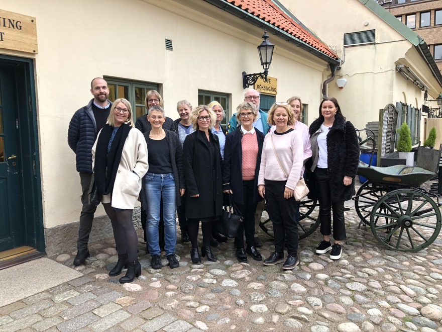 Tolv kvinnor och män som står tillsammans utanför ett café