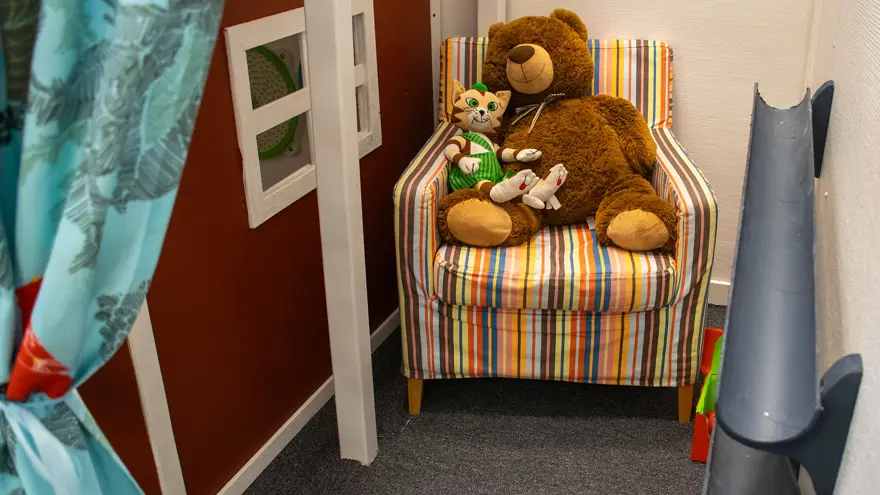 En fåtölj där en stor nalle och katten Findus sitter. Fåtöljen står i ett litet hörn, på ena sidan syns snickerboas röda vägg, på andra sidan två rör på väggen som man kan rulla bollar i.