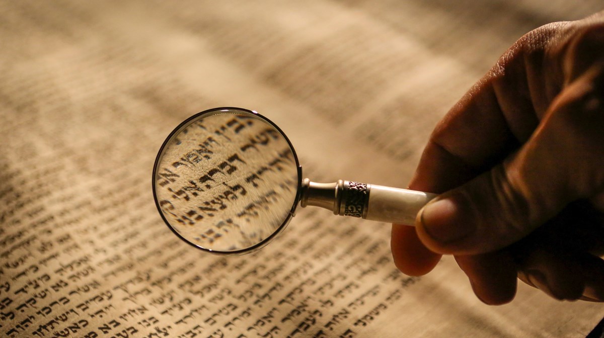 man ser ett förstoringsglas över hebreisk text på gammalt papper