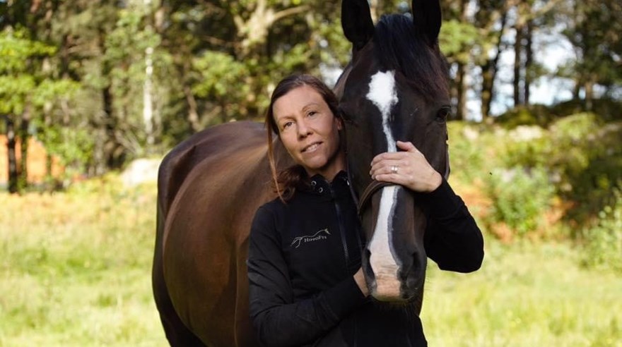 Porträtt på Nina Magnusson som står och håller händerna på en häst