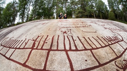 Två barn sitter på en bergsknalle som är täckt av en rödaktig hällristning