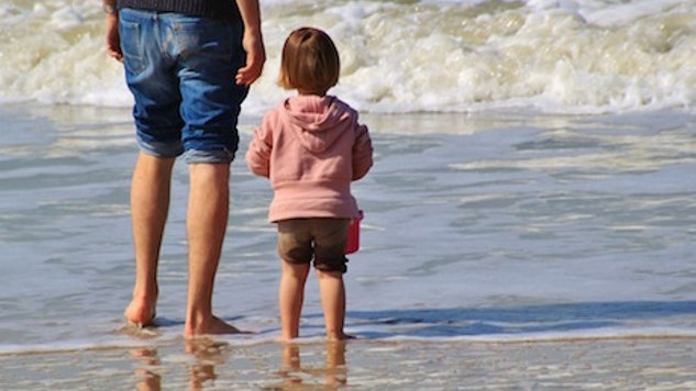 En vuxen och ett barn barfota vid  strandkant där vågor rullar in