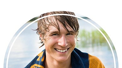En glad ungdom med handduk och blött hår vid en sjö.