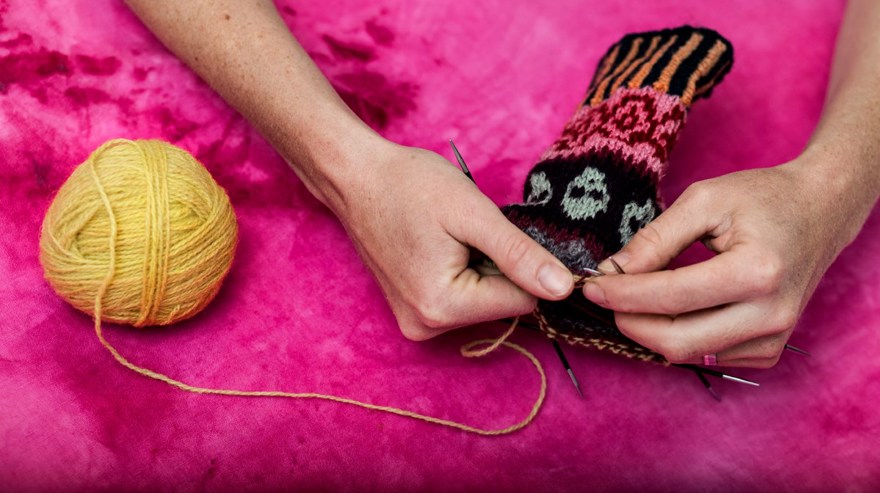 två händer som tvåändsstickar i olika färger